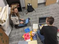 Two students describe and record objects from a psychological test, which include colorful blocks and a plastic baby doll
